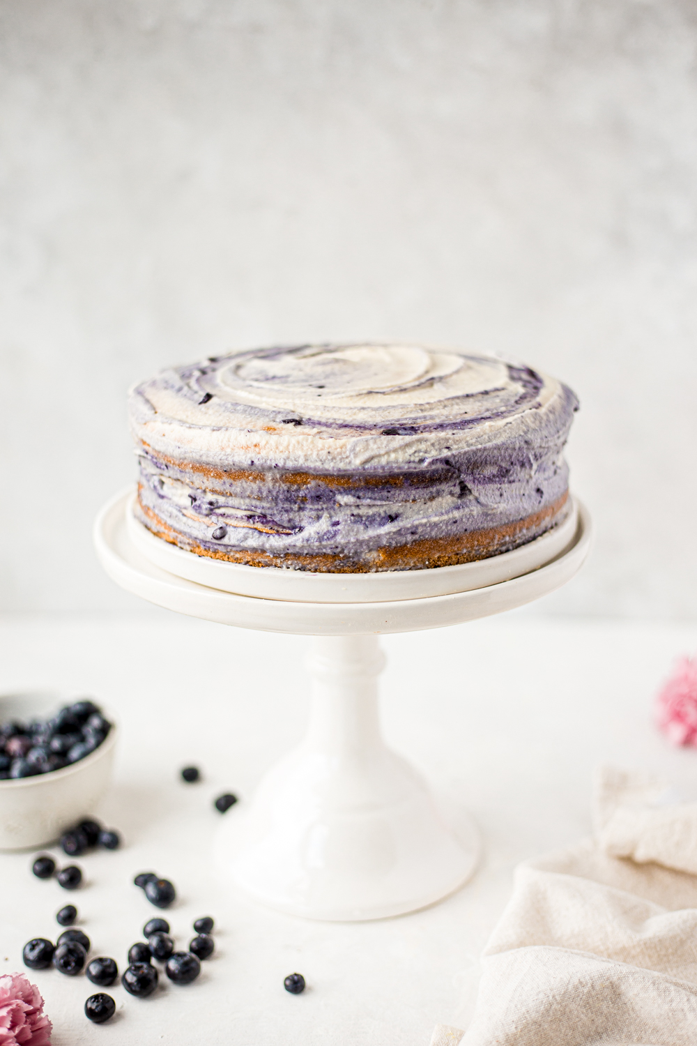 naked cake with white and purple frosting on a cake stand food photography