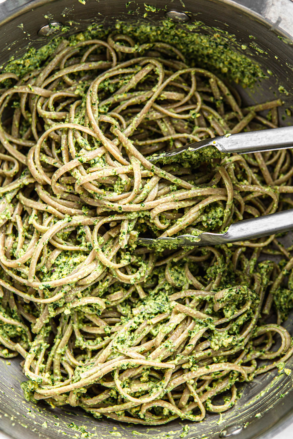 spaghetti tossed with green pesto sauce in a pot