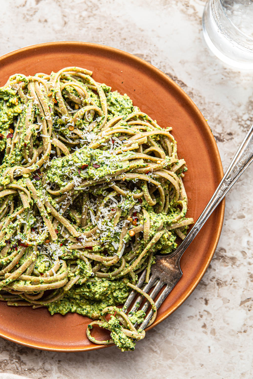 spaghetti with green pesto sauce on a plate with a fork