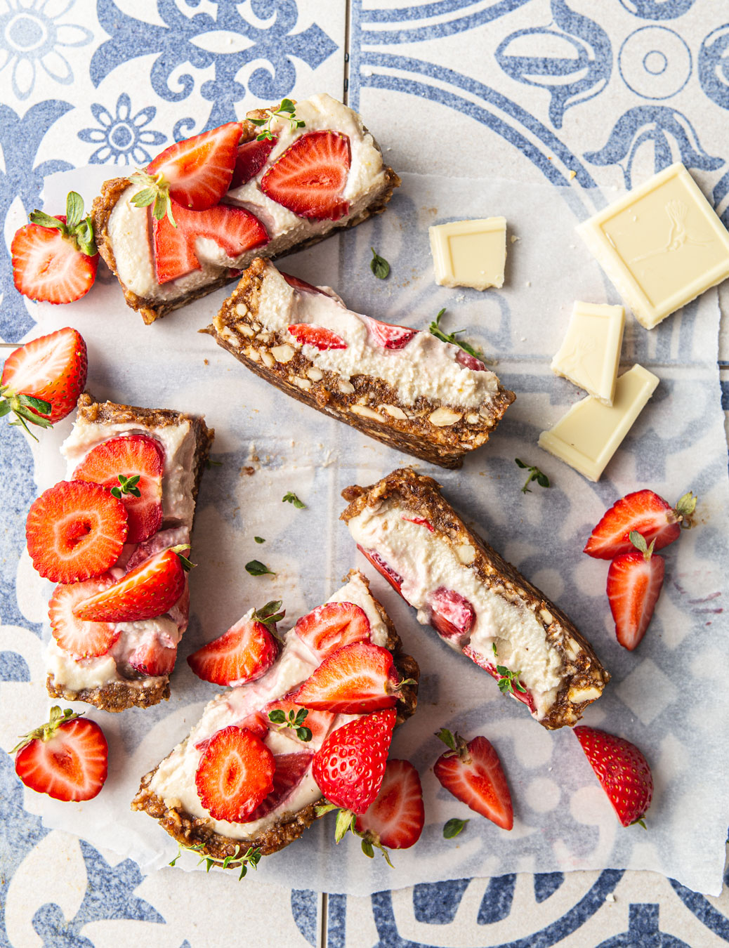 White Chocolate Cheesecake Bars with strawberries on blue tile backdrop